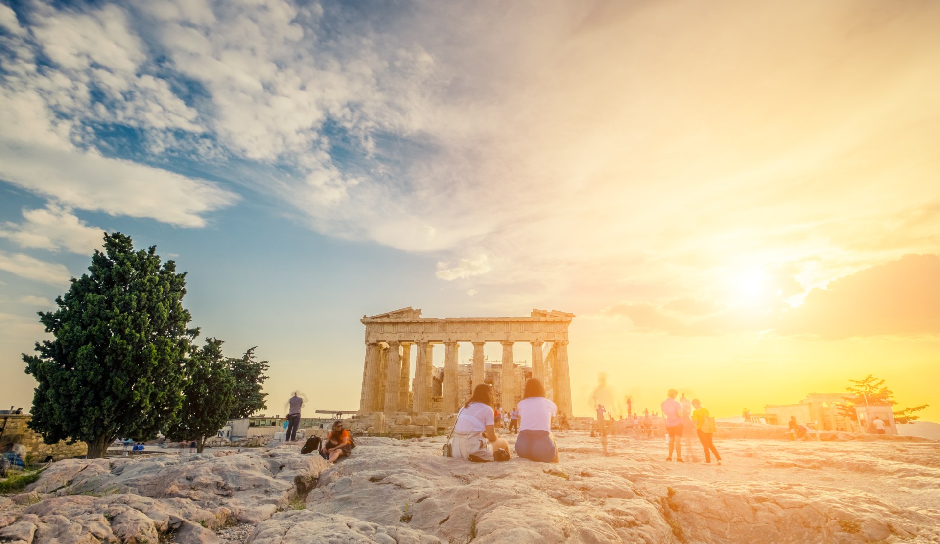 Young people sitting in front of the Parthenon on the Acropolis at sunset